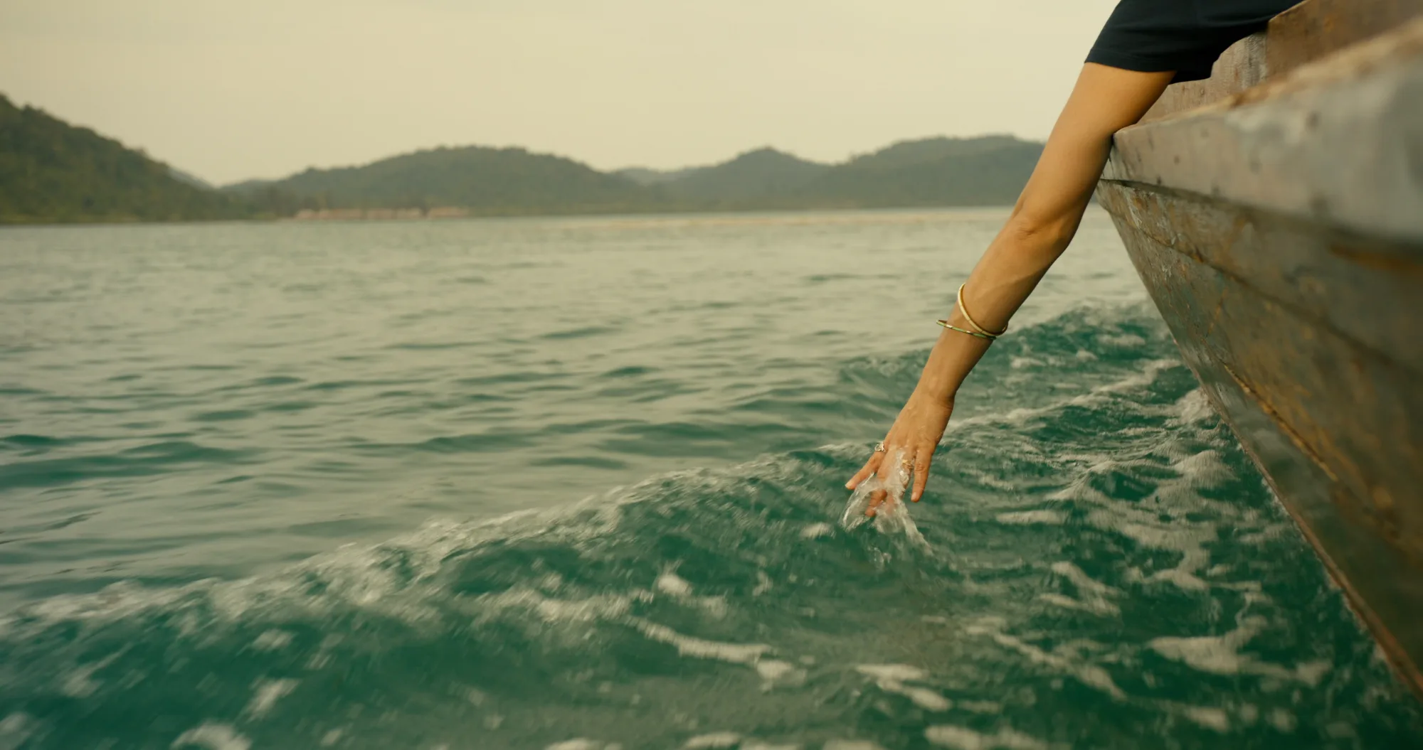 Hand skimming the sea surface from a traditional Telunas wooden boat during the crossing to the resort