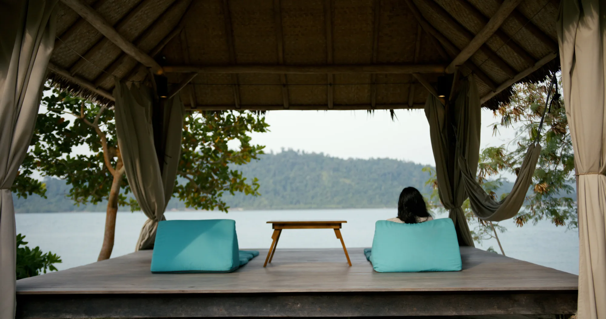 An open-sided waterfront pavilion with daybeds and a calm view across the water.