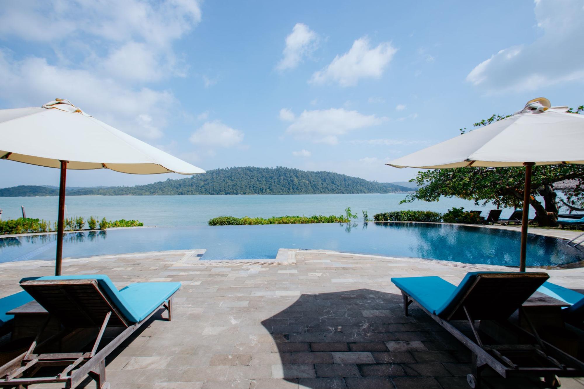 a pool with chairs and umbrellas by a body of water